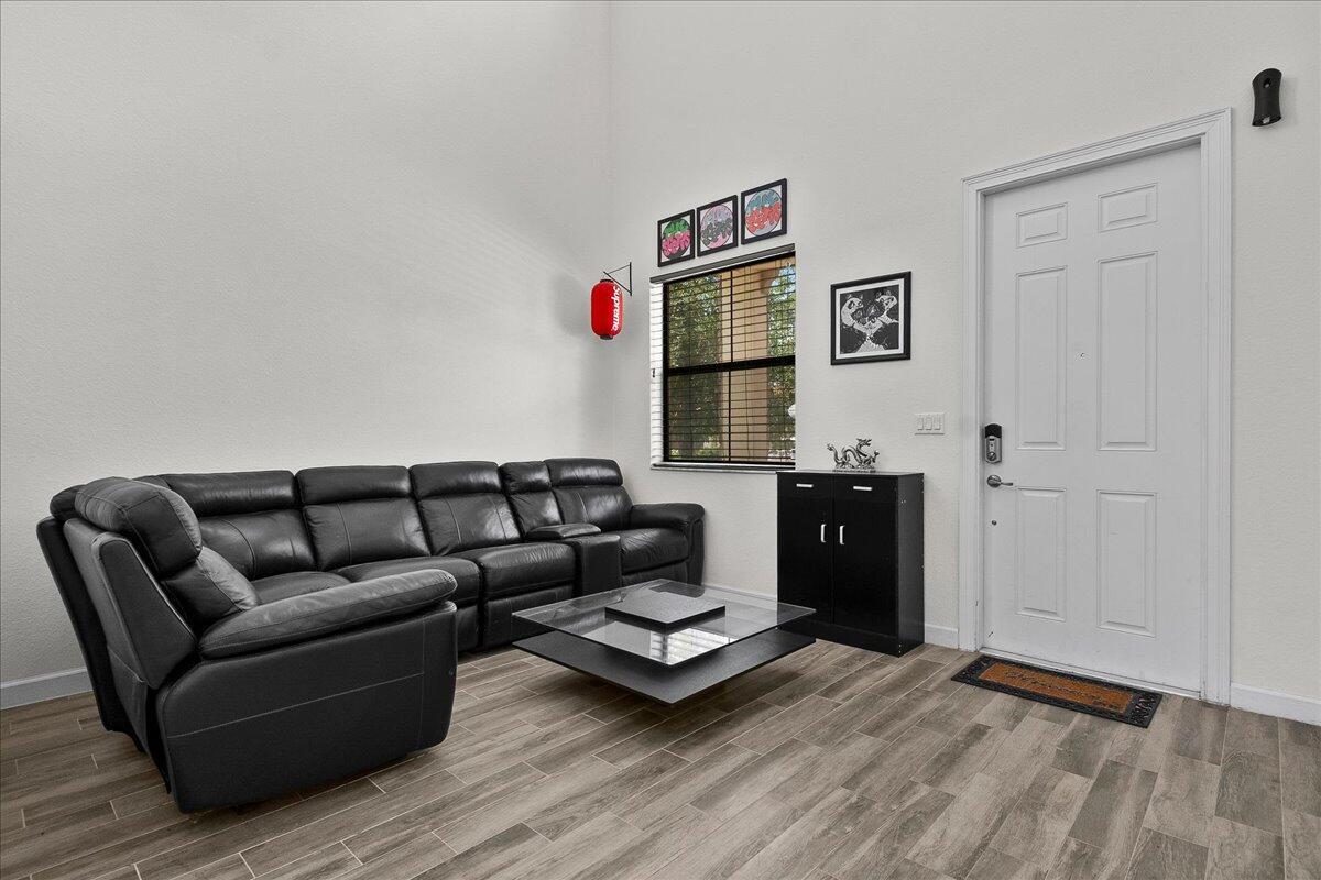 A living room features a black leather sectional, a glass coffee table, and wood-look flooring — 6021 Night Heron Court, FL 33415, FL