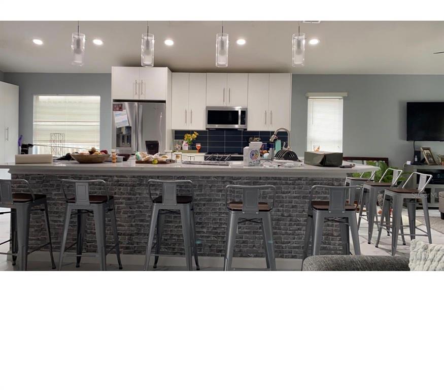 A kitchen features white cabinetry, a brick-faced island with metal bar stools, and pendant lighting — 2290 COBBLEFIELD CIRCLE, APOPKA, FL