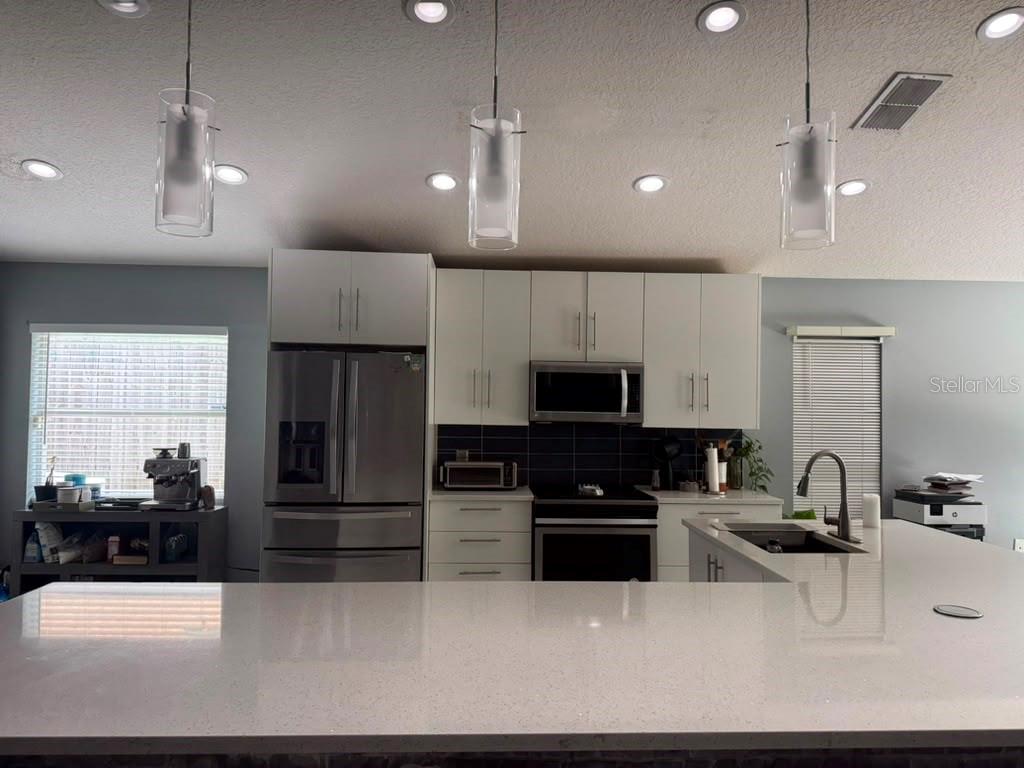 A modern kitchen features white cabinetry, stainless steel appliances, and a large quartz-topped island — 2290 COBBLEFIELD CIRCLE, APOPKA, FL