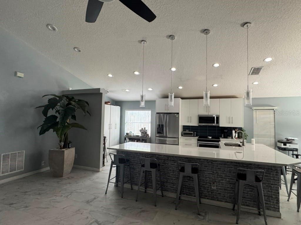 A modern kitchen features a large island with bar seating, white cabinets, and pendant lighting — 2290 COBBLEFIELD CIRCLE, APOPKA, FL