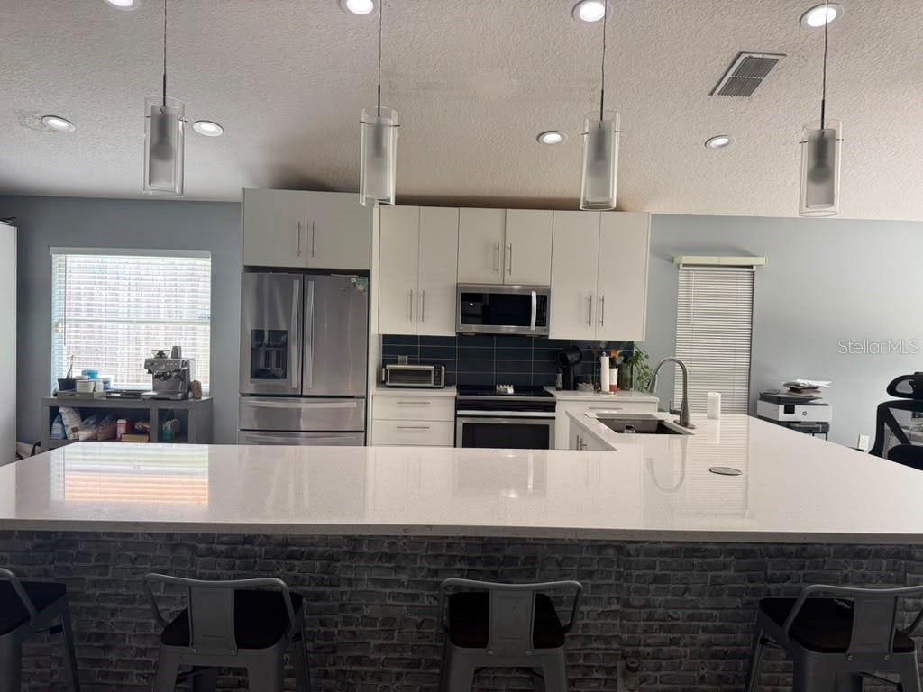 A modern kitchen features white cabinets, a large quartz island, and a gray brick base — 2290 COBBLEFIELD CIRCLE, APOPKA, FL