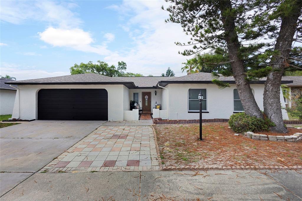 A single-story white house with a black garage door and a paved walkway — 10951 PEPPERTREE LN, PORT RICHEY,, FL