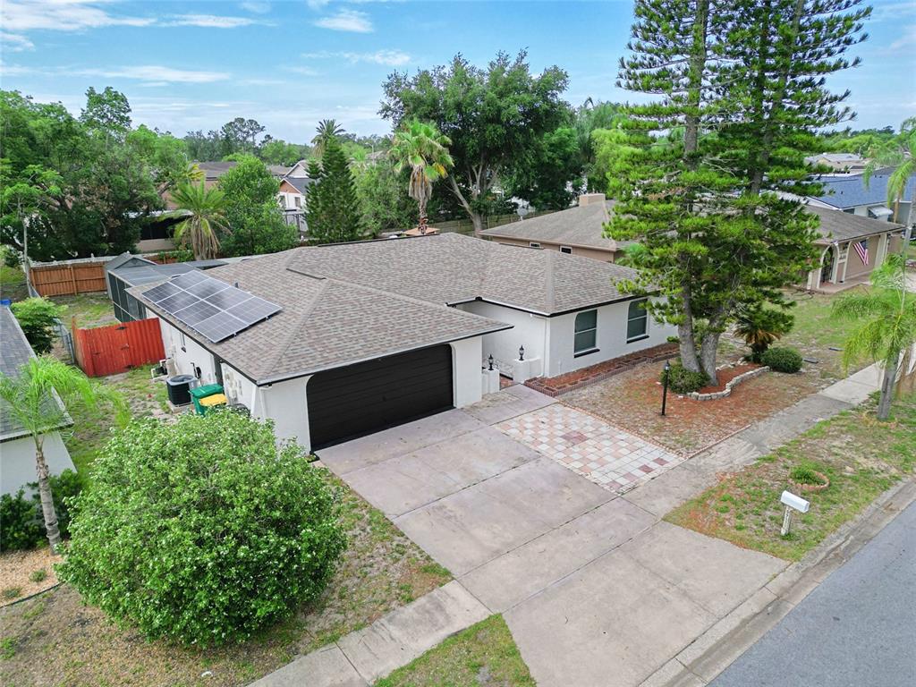 An aerial view shows a single-story house with a dark garage door and solar panels — 10951 PEPPERTREE LN, PORT RICHEY,, FL