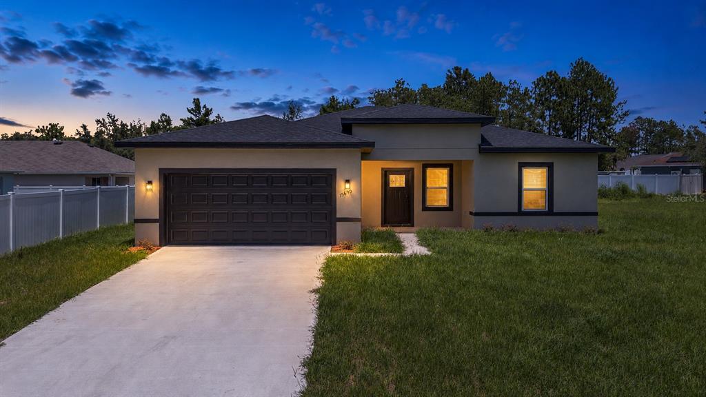 A single-story house with a dark garage door and exterior lighting at dusk — 15690 SW 49TH AVENUE ROAD, OCALA, FL