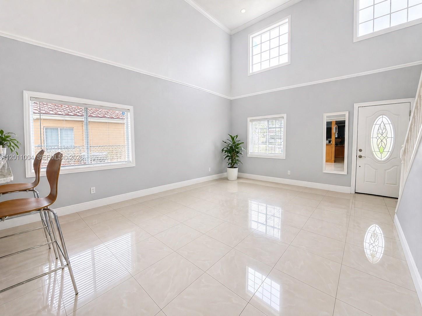A bright, high-ceilinged room features light gray walls, large windows, and polished tile flooring — 10290 SW 24th Ct, Miramar FL 33025, MIRAMAR, FL