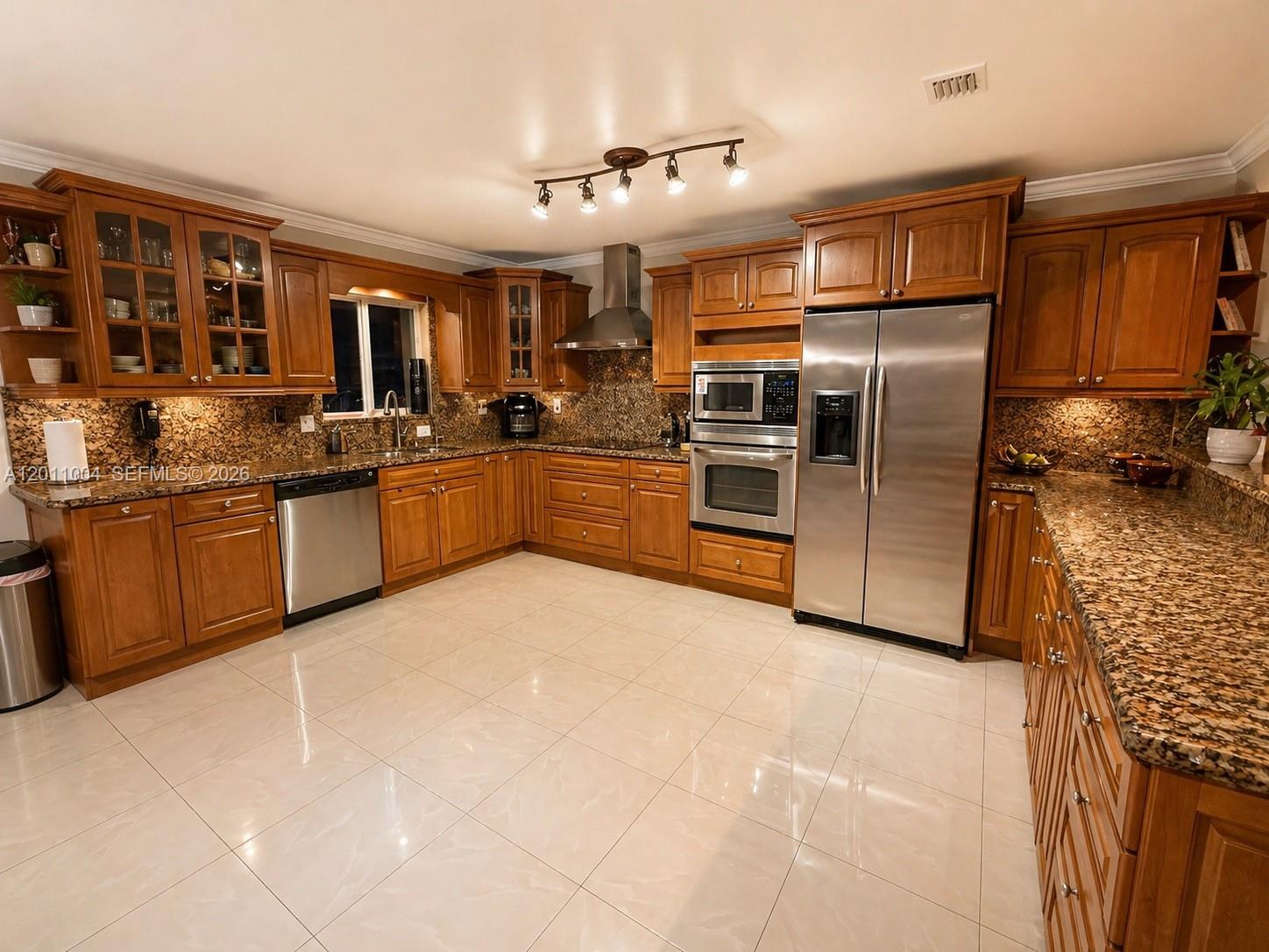 A kitchen features wood cabinets, granite countertops, stainless steel appliances, and light-colored tile flooring — 10290 SW 24th Ct, Miramar FL 33025, MIRAMAR, FL