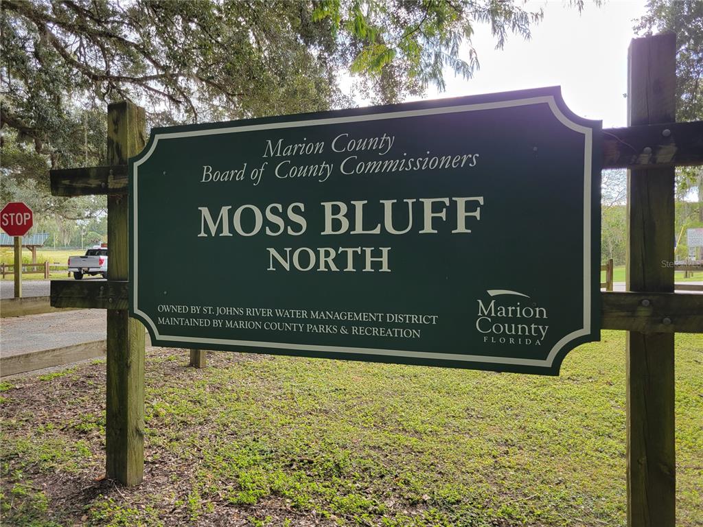 A green sign for Moss Bluff North park stands on wooden posts in a wooded area — TBD SE 170 AVE ROAD UNIT Tract A, OCKLAWAHA, FL