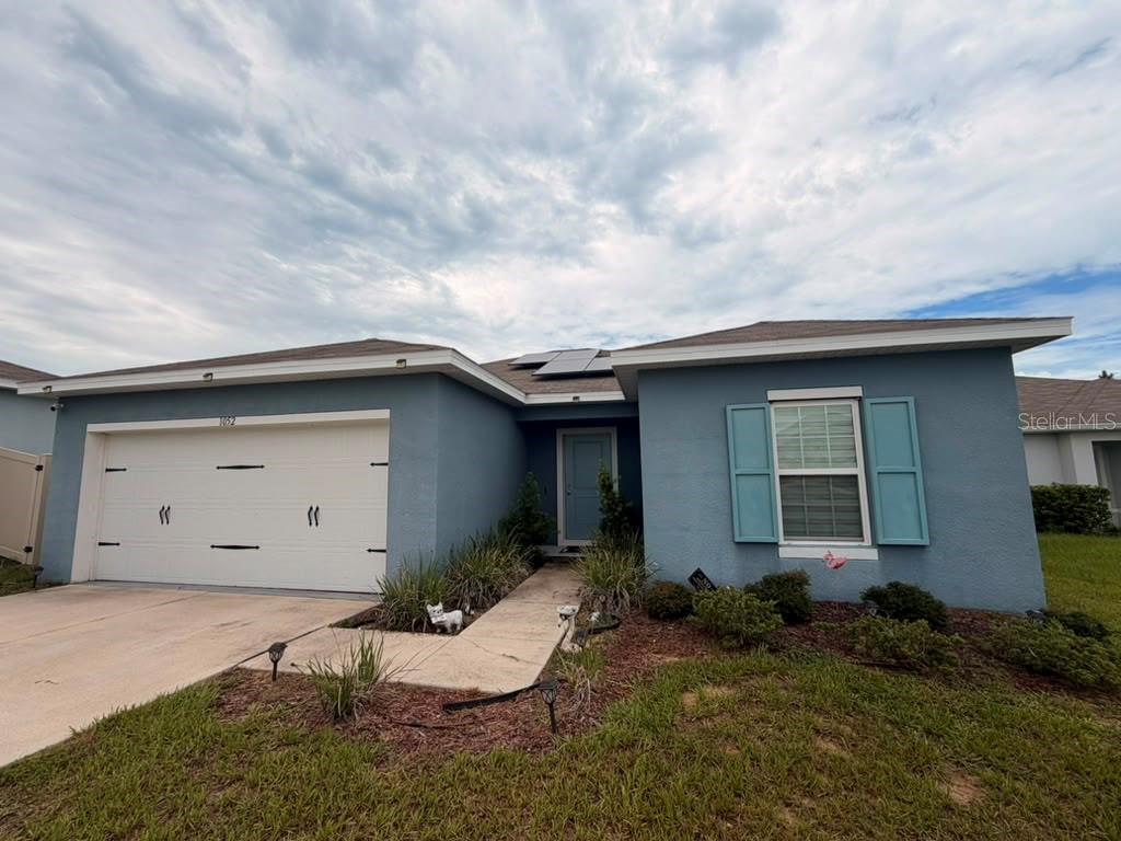 A single-story house with blue stucco siding, a white garage door, and solar panels — 1052 KOBUK STREET, HAINES CITY, FL