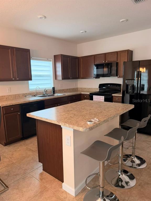 A kitchen features dark wood cabinets, a laminate island with bar stools, and black appliances — 1052 KOBUK STREET, HAINES CITY, FL