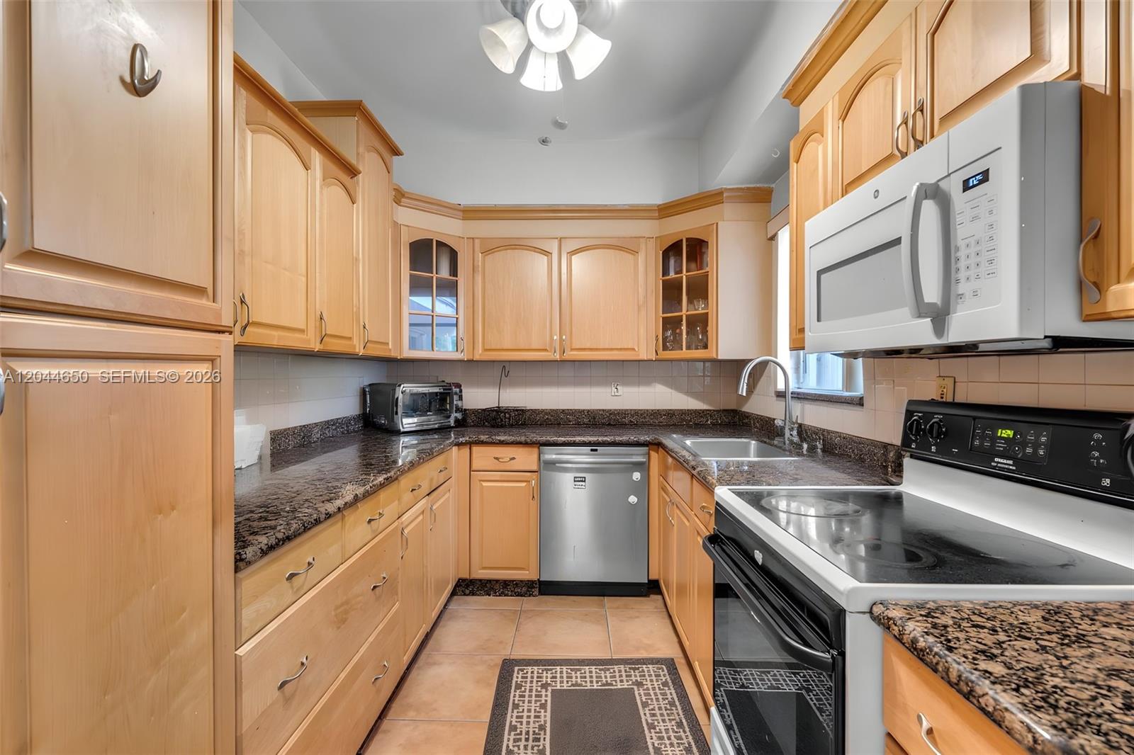 A kitchen features light wood cabinets, dark granite countertops, stainless steel appliances, and tile flooring — 1439 Miller Rd, Coral Gables FL 33146, CORAL GABLES, FL