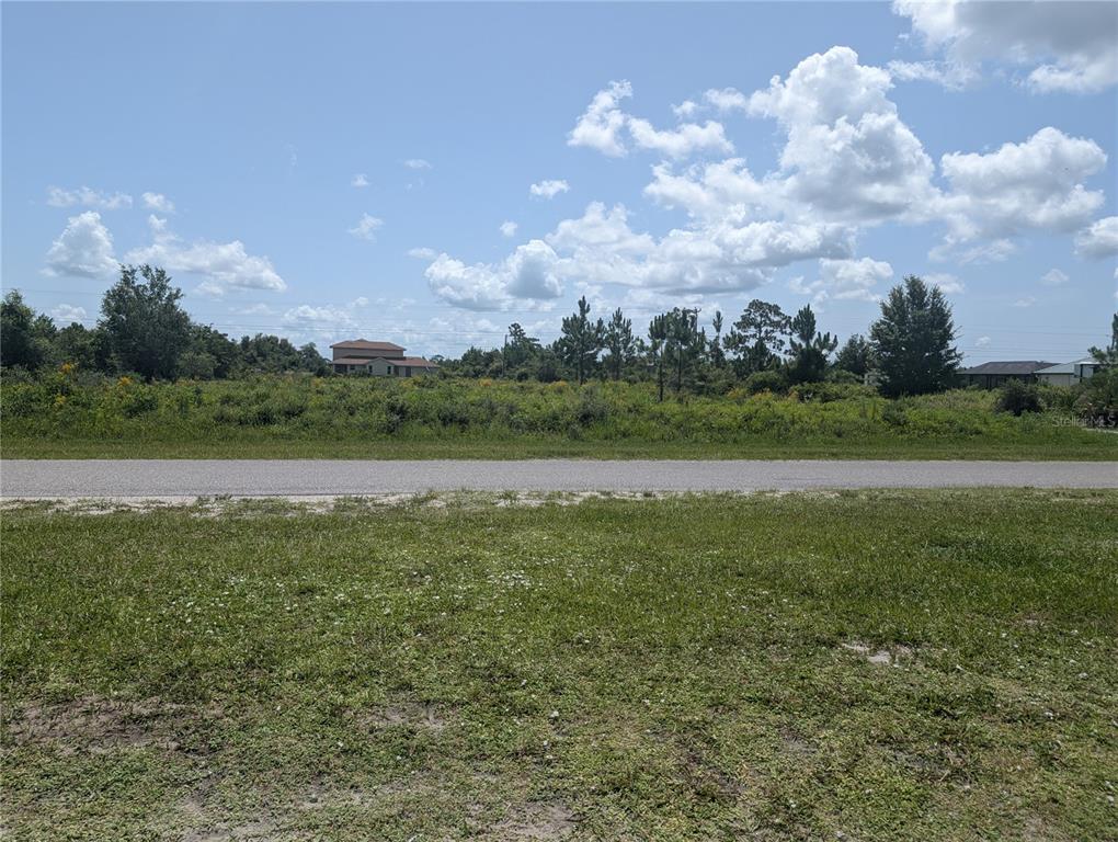 A grassy foreground leads to a paved road and an undeveloped, brush-covered vacant lot — 96 DESOTO AVENUE, INDIAN LAKE ESTATES, FL