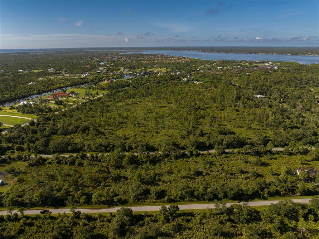 An aerial view shows a large, undeveloped wooded lot with a road in the foreground — 13211 CHIMINIELLO DRIVE, PORT CHARLOTTE, FL