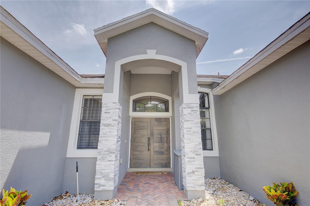 The exterior of a house features a stone-accented entryway with double wooden doors — 2407 FOLIAGE OAK TERRACE, OVIEDO, FL