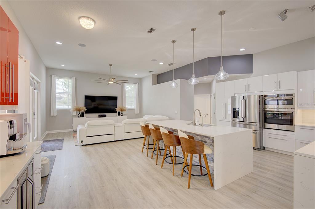 A modern open-concept kitchen and living area featuring a large island, white cabinetry, and flooring — 2407 FOLIAGE OAK TERRACE, OVIEDO, FL