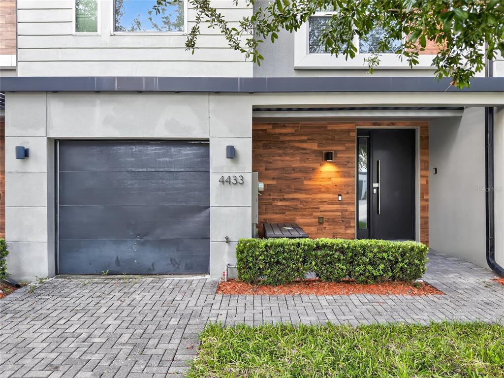 A modern townhome exterior features a gray garage, wood-paneled entryway, and a paved driveway — 4433 LE REVE COURT, KISSIMMEE, FL