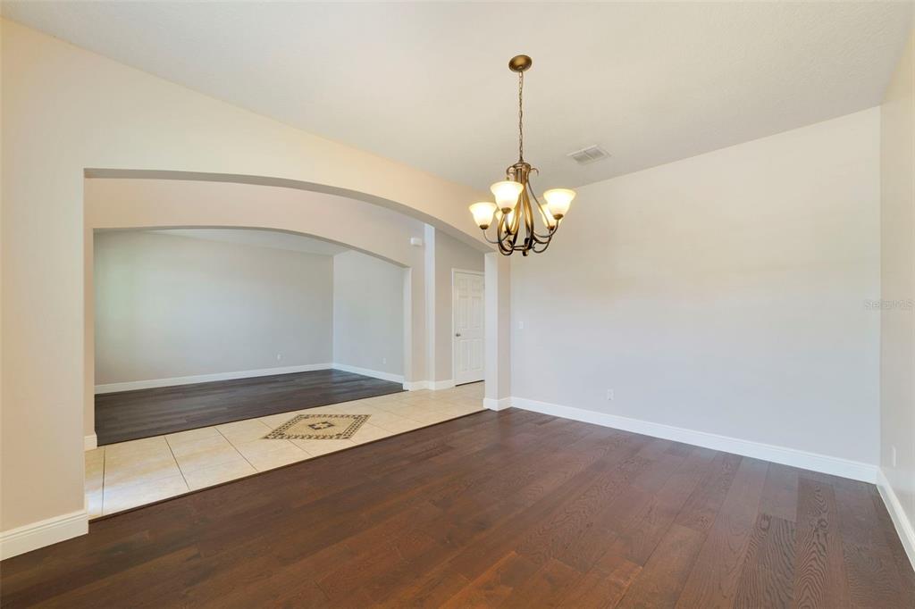 A dining room with dark wood flooring, a chandelier, and an arched entryway — 4958 CYPRESS HAMMOCK DRIVE, ST CLOUD, FL
