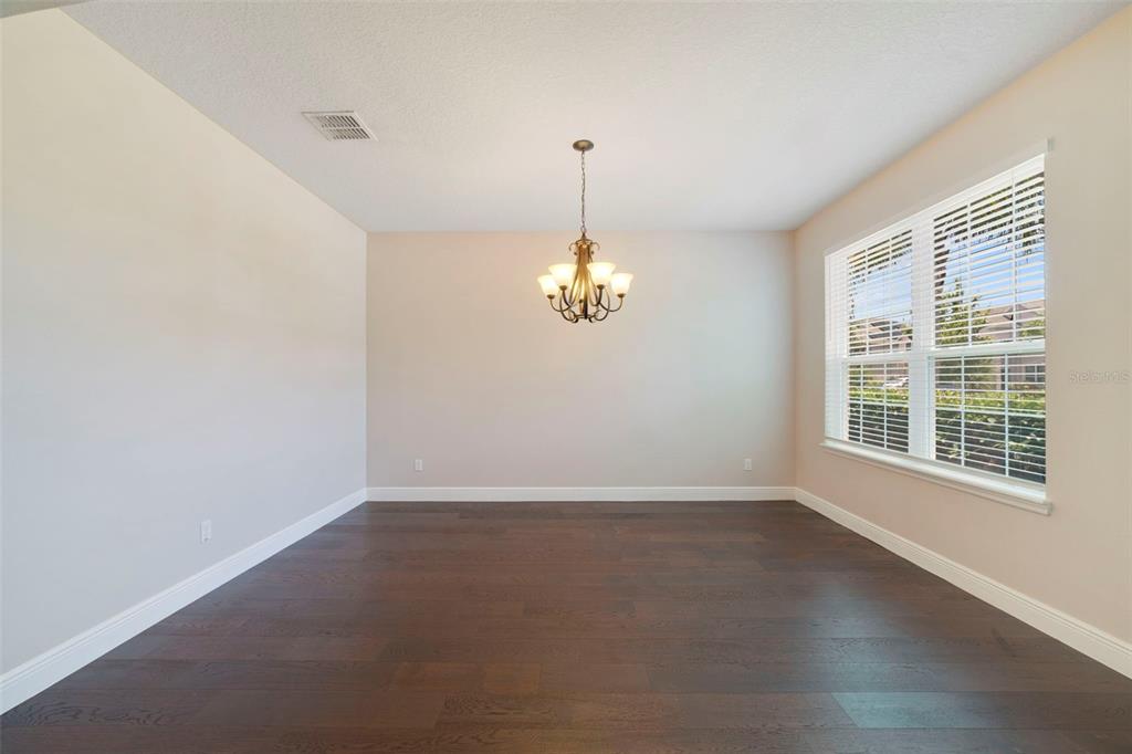 An empty dining room features dark hardwood floors, a chandelier, and a large window — 4958 CYPRESS HAMMOCK DRIVE, ST CLOUD, FL