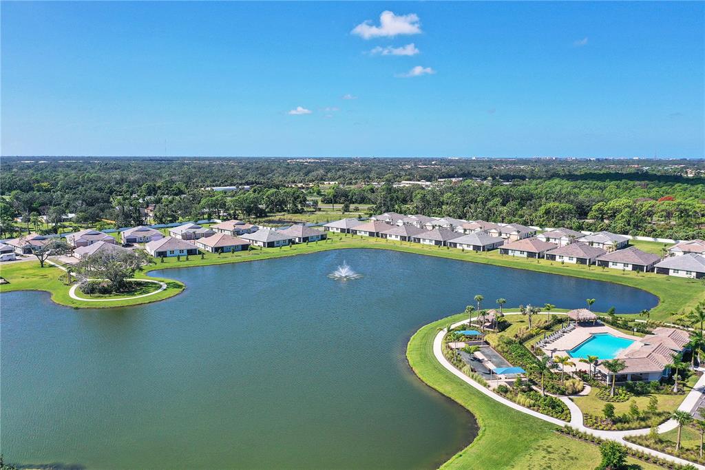 An aerial view shows a residential community with houses surrounding a lake and pool area — 305 IBIZA LOOP, VENICE, FL