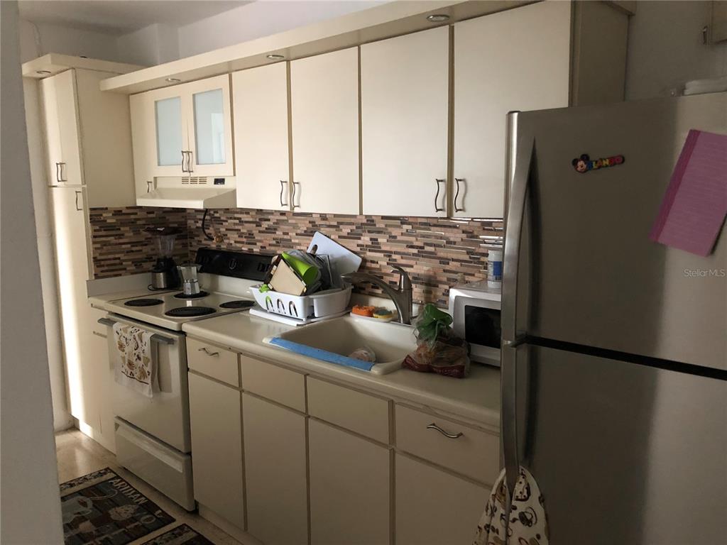 A kitchen features off-white cabinets, a tiled backsplash, a stainless steel refrigerator, and a stove — 274 CALLE URUGUAY UNIT 202, SAN JUAN, PR