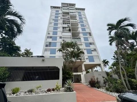 A tall, multi-story apartment building with balconies stands behind a low wall and palm trees — 274 CALLE URUGUAY UNIT 202, SAN JUAN, PR