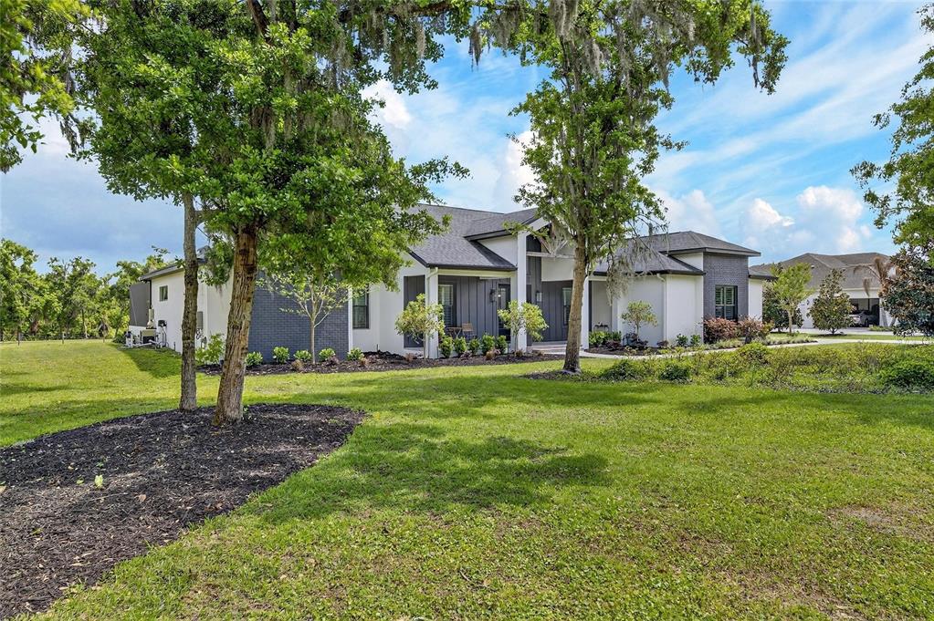 A modern single-story house with white and dark gray exterior walls sits on a lawn — 16410 ALDERMAN TURNER ROAD, WIMAUMA, FL