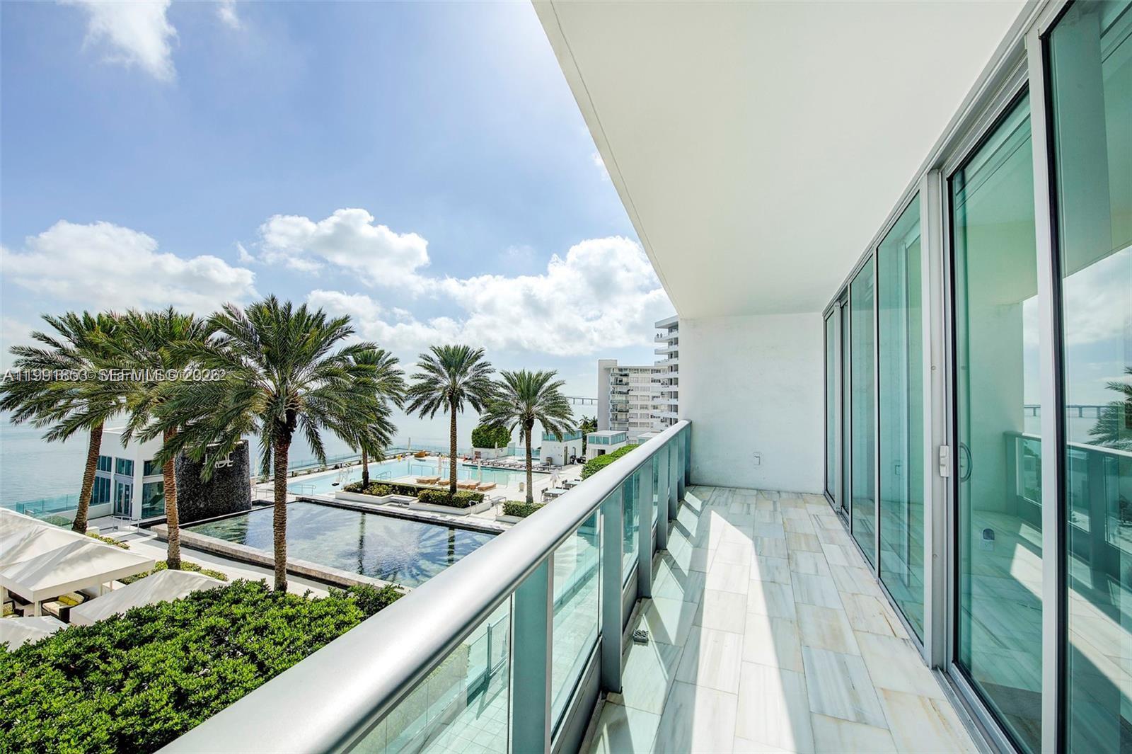 A balcony with glass railings overlooks a swimming pool, palm trees, and the ocean — 1331 Brickell Bay Dr # 903, Miami FL 33131, MIAMI, FL