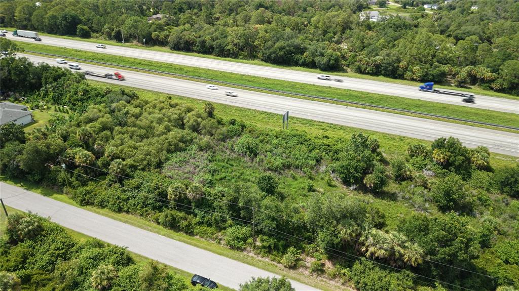 An aerial view shows a vacant, wooded lot situated between a paved road and a highway — SNUG STREET, NORTH PORT, FL