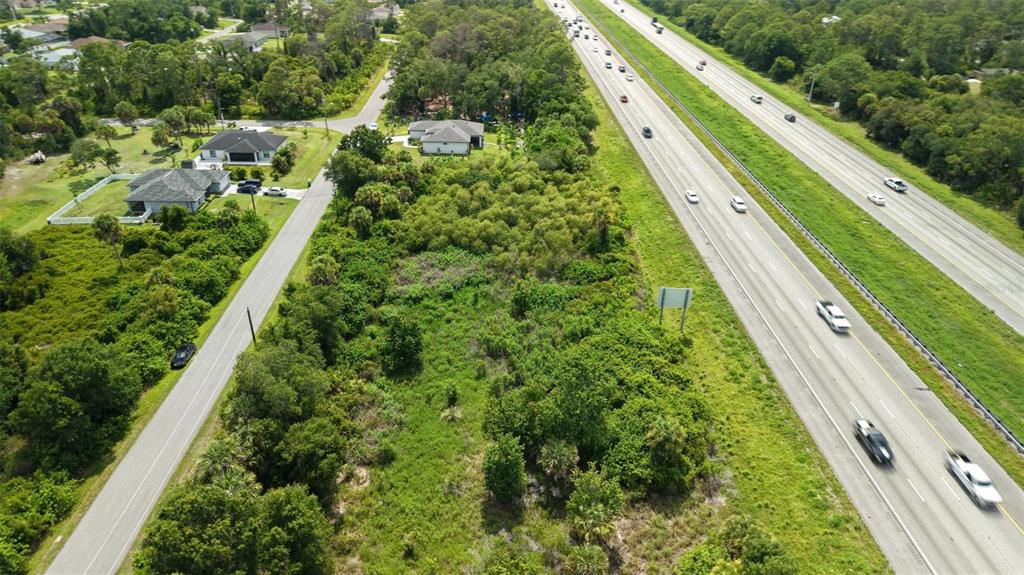 An aerial view shows a vacant, wooded lot situated between a residential road and highway — SNUG STREET, NORTH PORT, FL