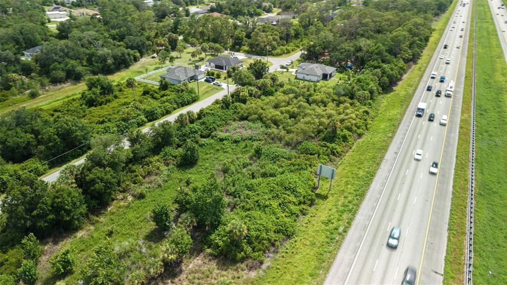 An aerial view shows a vacant, tree-covered lot adjacent to a multi-lane highway — SNUG STREET, NORTH PORT, FL