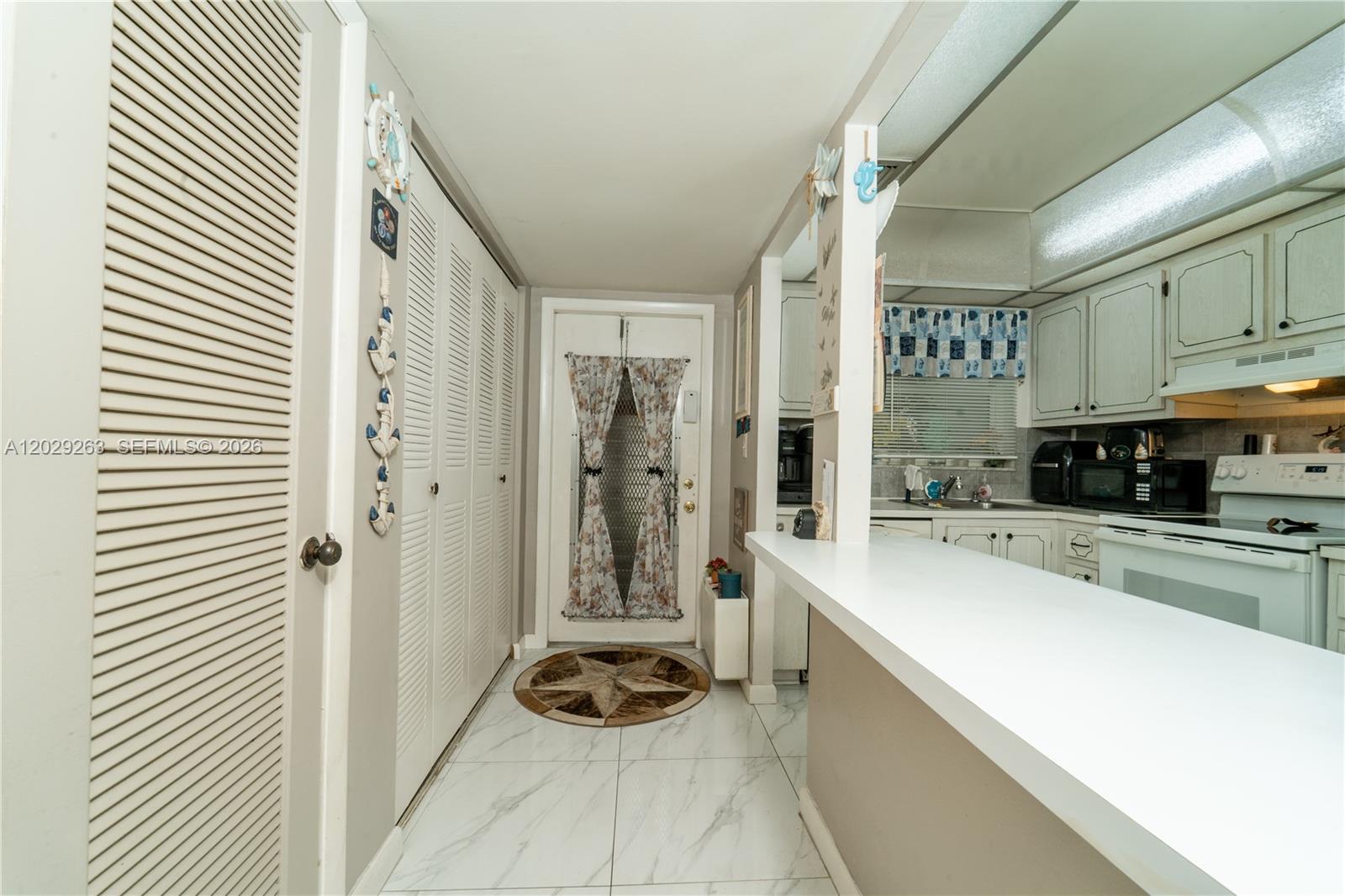 A kitchen with white cabinets and a breakfast bar opens into a tiled entryway — 2811 N Pine Island Rd # 102, Sunrise FL 33322, SUNRISE, FL