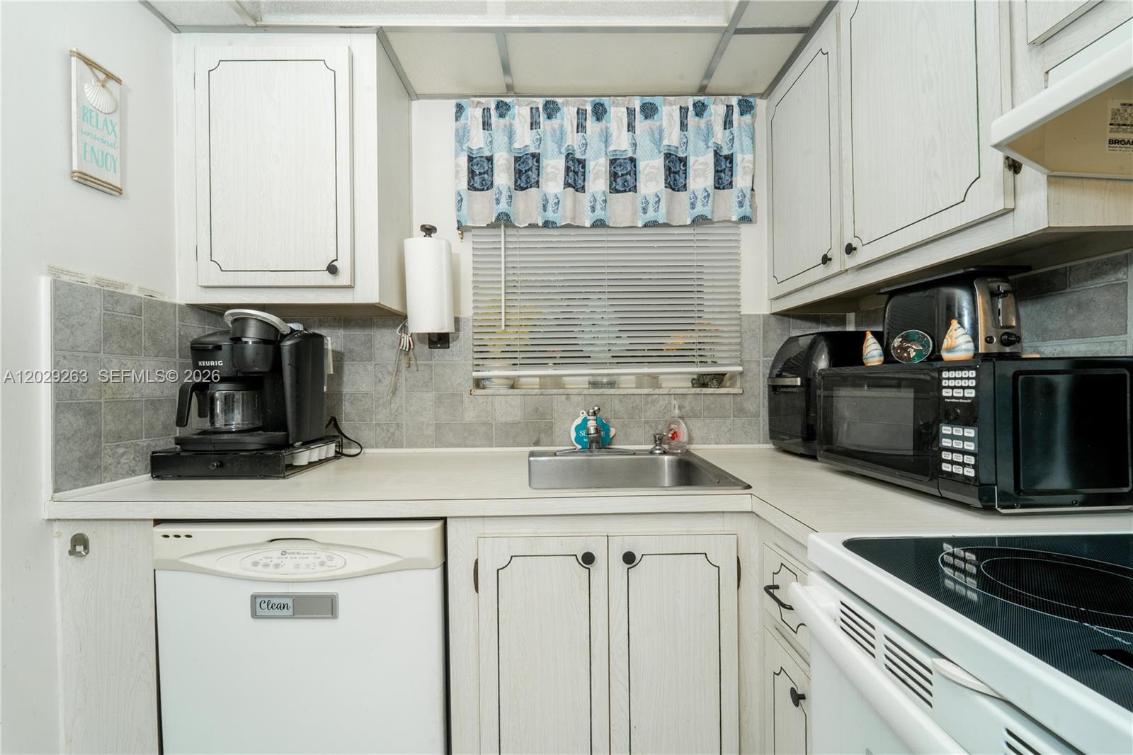 A kitchen features white cabinets, a stainless steel sink, and a tiled backsplash — 2811 N Pine Island Rd # 102, Sunrise FL 33322, SUNRISE, FL