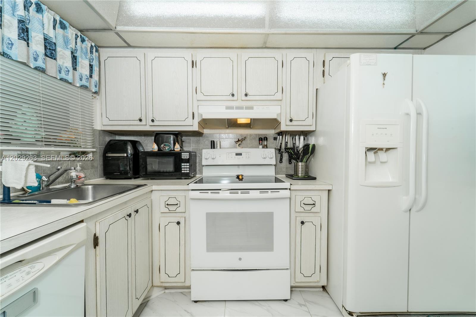 A kitchen features white cabinetry, white appliances, a stainless steel sink, and a tiled backsplash — 2811 N Pine Island Rd # 102, Sunrise FL 33322, SUNRISE, FL