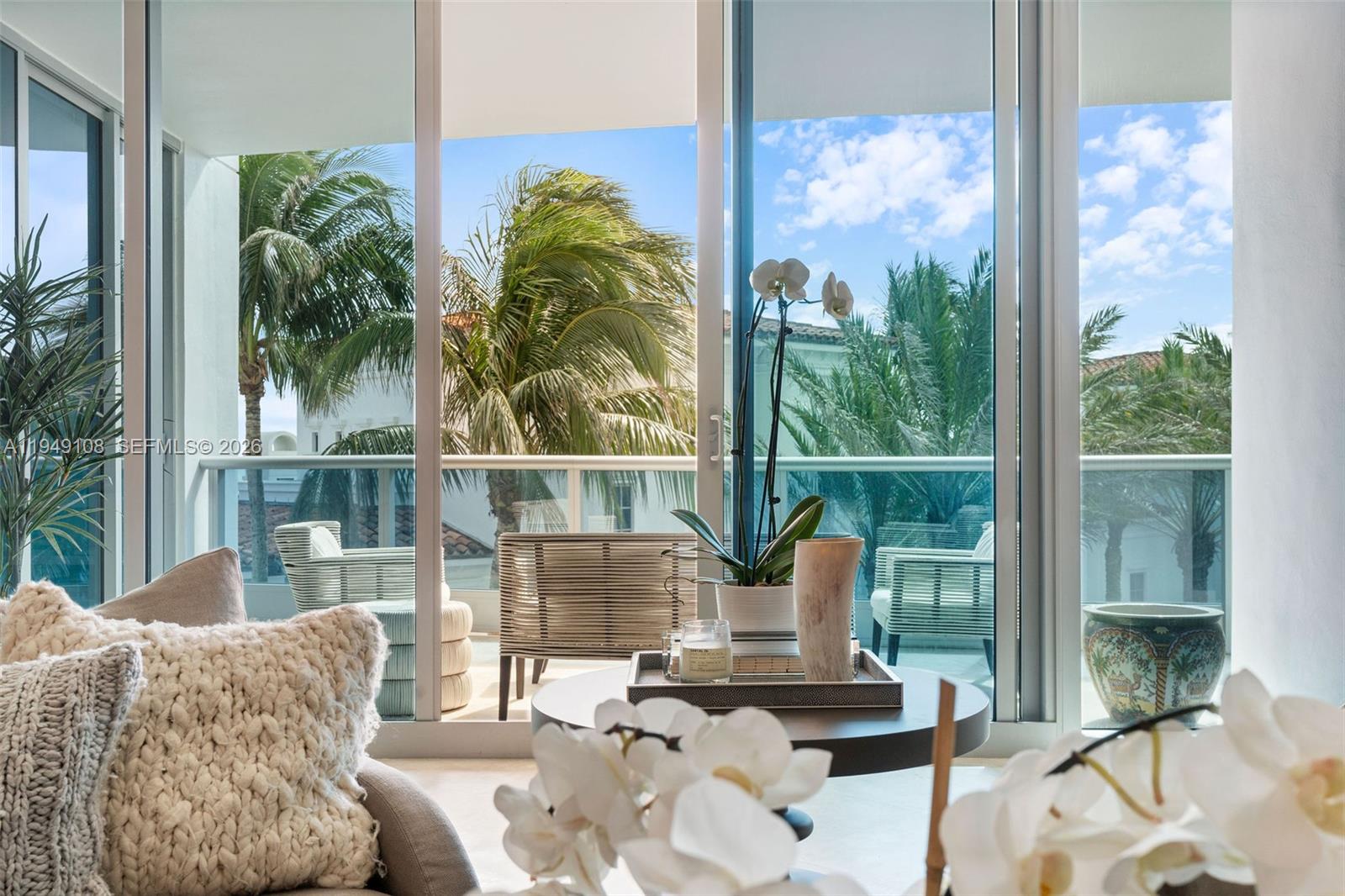A living room with large glass sliding doors opens onto a balcony with palm trees — 5959 Collins Ave # 606, Miami Beach FL 33140, MIAMI BEACH, FL