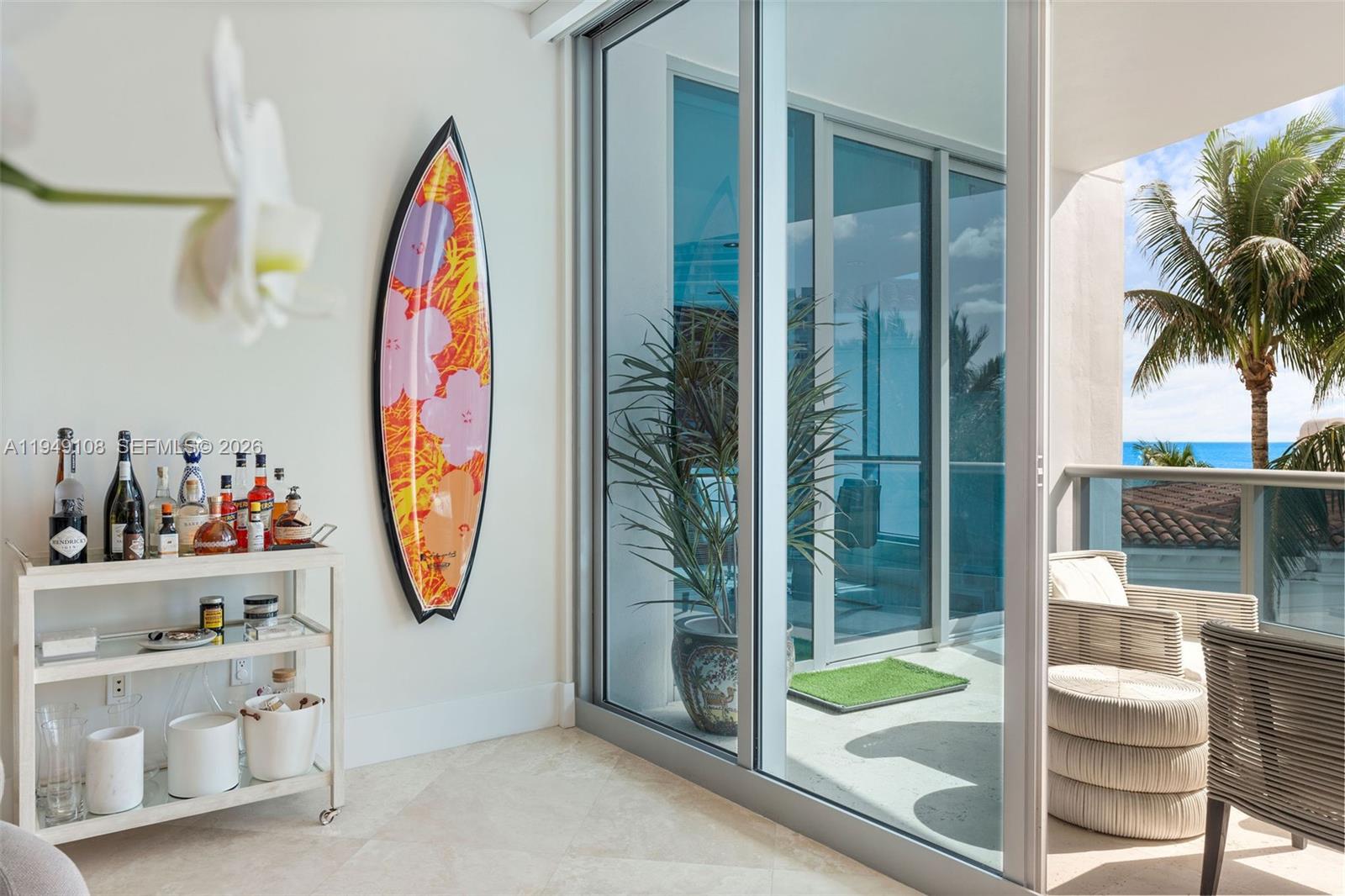 A room with a bar cart, a decorative surfboard on the wall, and a balcony view — 5959 Collins Ave # 606, Miami Beach FL 33140, MIAMI BEACH, FL