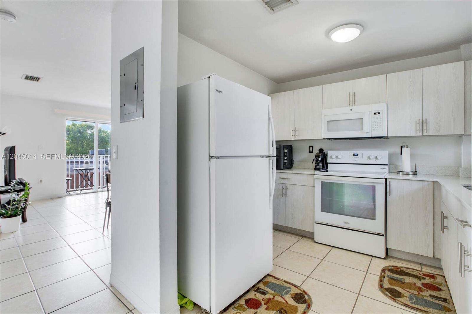 A kitchen features white appliances, light wood-grain cabinets, and tile flooring, opening to a living area — 1349 SW 3rd St # 7, Miami FL 33135, MIAMI, FL