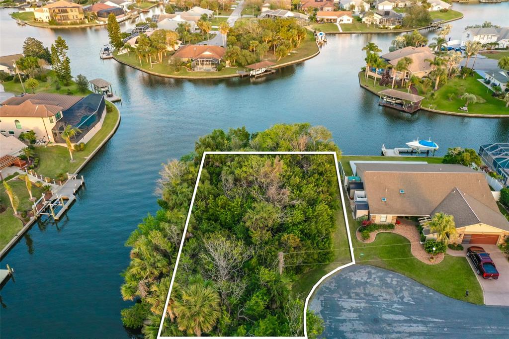 An aerial view shows a vacant, tree-covered waterfront lot outlined in white next to houses — 44 CLOVERDALE COURT N, PALM COAST, FL