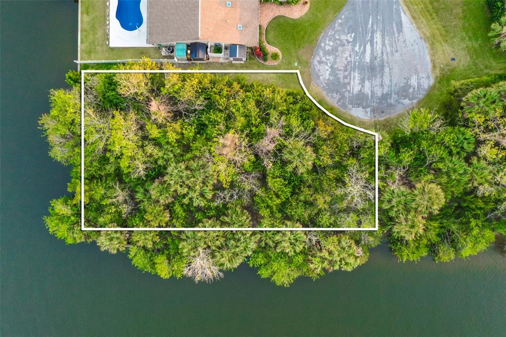 An aerial view shows a vacant, tree-covered waterfront lot outlined in white next to a house — 44 CLOVERDALE COURT N, PALM COAST, FL