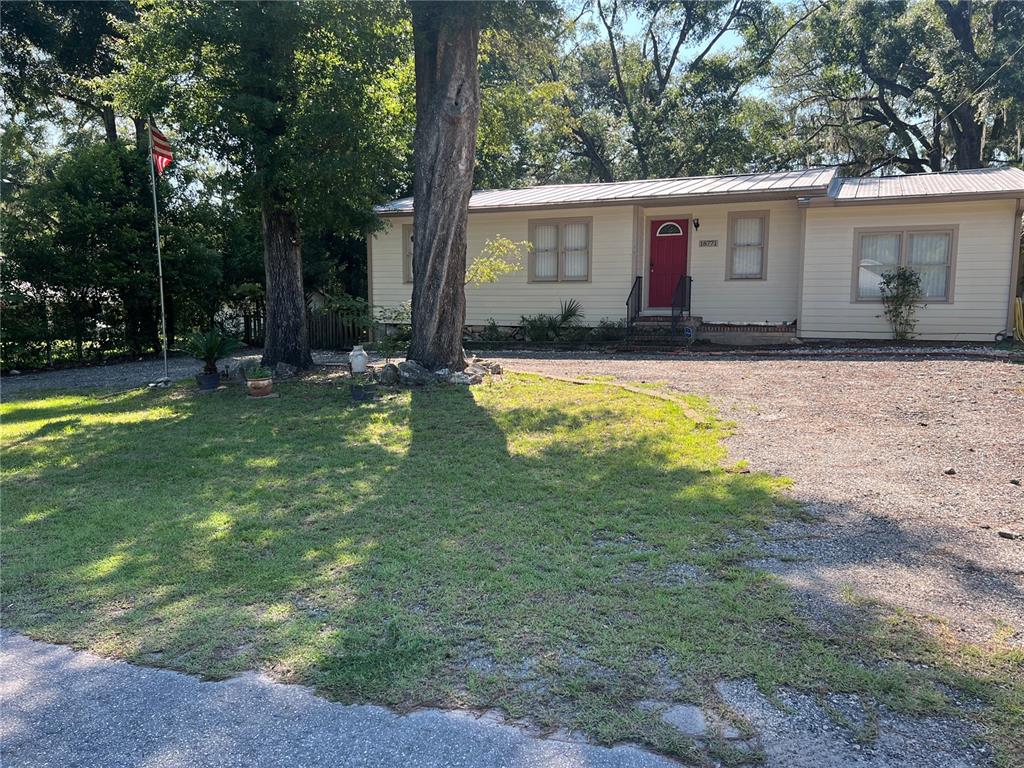 A single-story house with light siding and a red front door sits behind a gravel driveway — 18771 NW 244TH STREET, HIGH SPRINGS, FL
