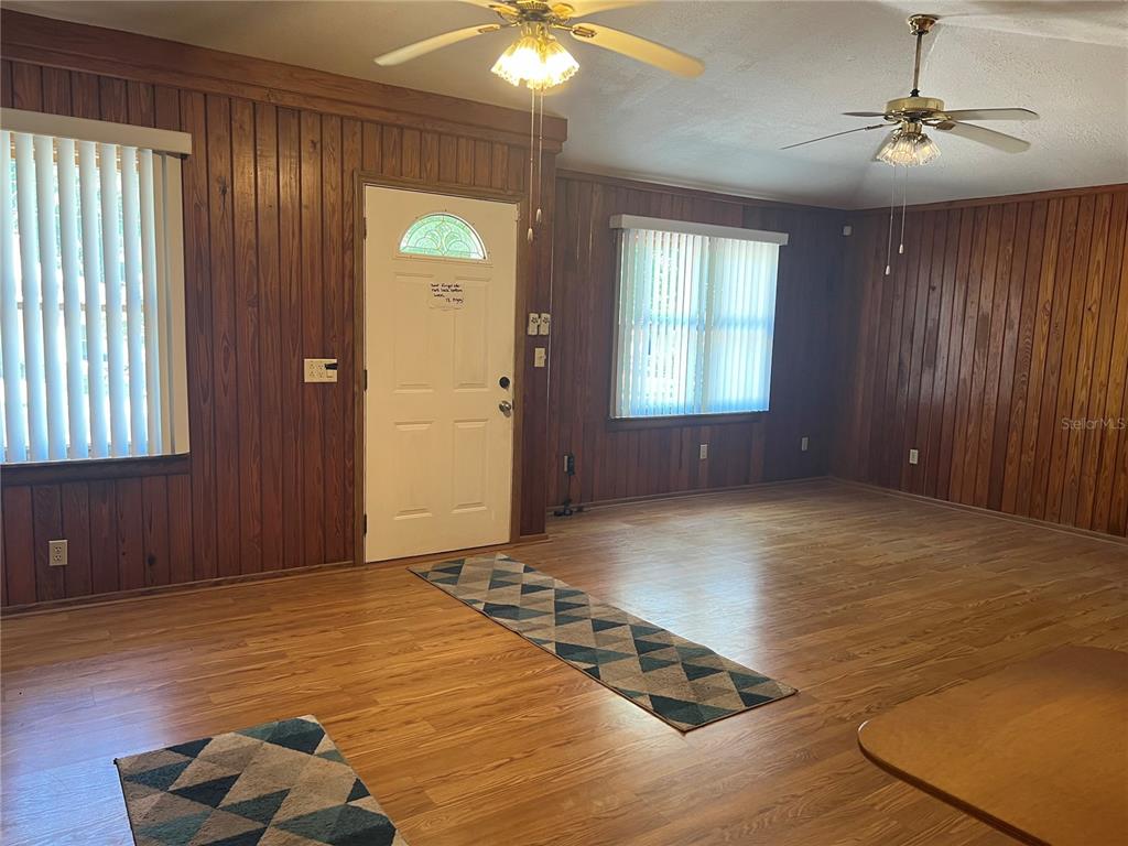 A living room features wood-paneled walls, light wood flooring, two ceiling fans, and vertical blinds — 18771 NW 244TH STREET, HIGH SPRINGS, FL