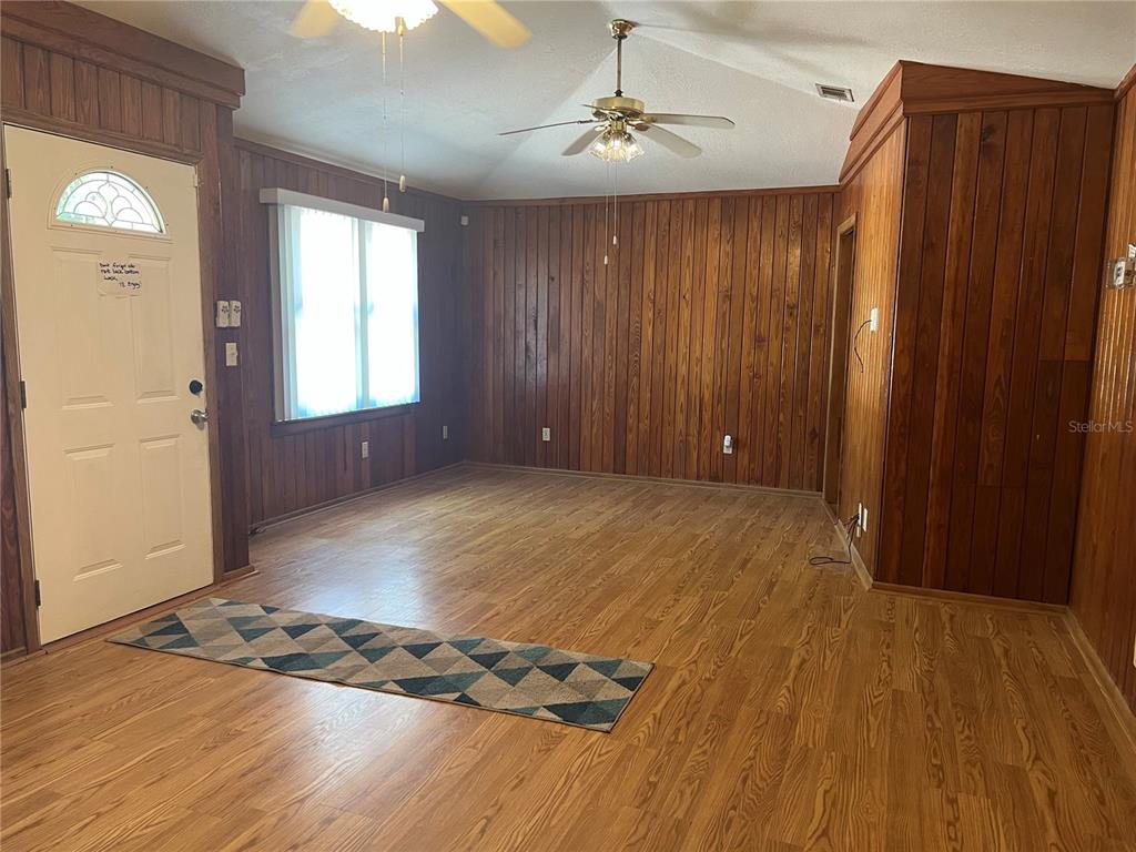 A living room features wood-paneled walls, wood-look flooring, a vaulted ceiling, and a ceiling fan — 18771 NW 244TH STREET, HIGH SPRINGS, FL