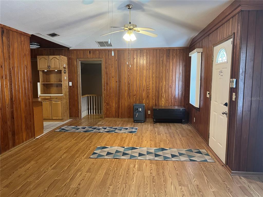 A living room features wood-paneled walls, wood-look flooring, a ceiling fan, and a front door — 18771 NW 244TH STREET, HIGH SPRINGS, FL