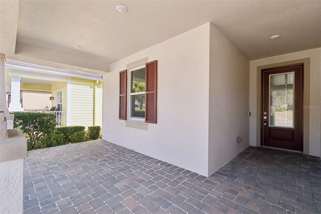A covered entryway features brick pavers, a brown front door, and a window with shutters — 19474 LILY POND COURT, BROOKSVILLE, FL
