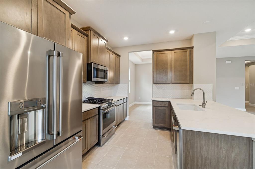A modern kitchen features stainless steel appliances, wood cabinetry, and a white quartz island countertop — 19474 LILY POND COURT, BROOKSVILLE, FL