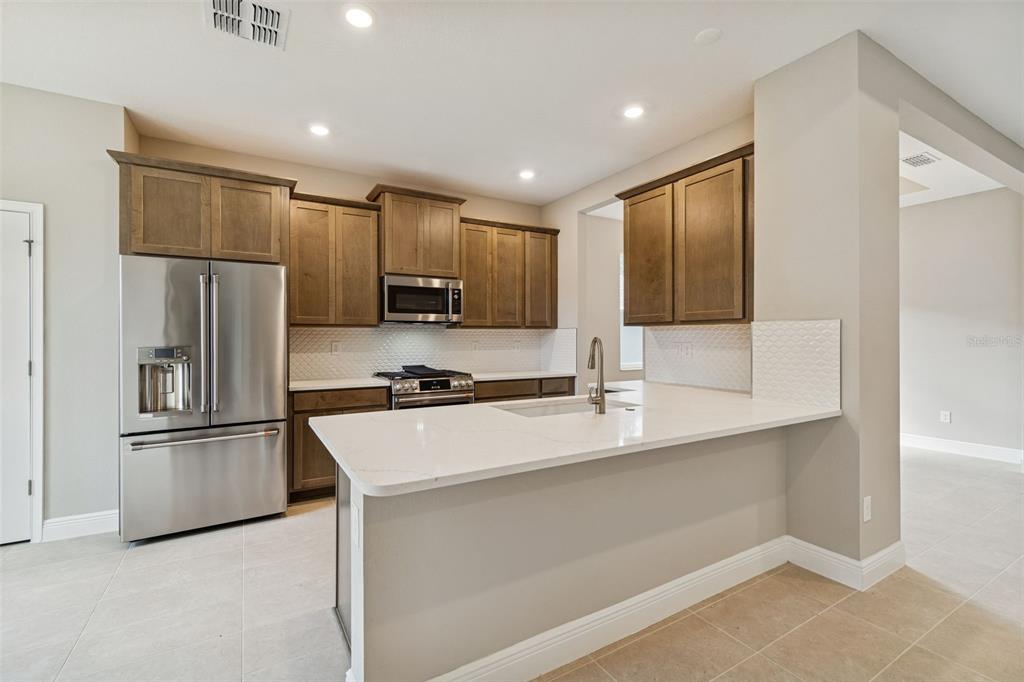A modern kitchen features wood cabinets, stainless steel appliances, and a white quartz breakfast bar — 19474 LILY POND COURT, BROOKSVILLE, FL