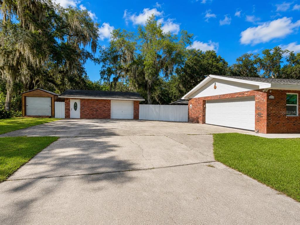 A brick house and detached garage with a large concrete driveway under a blue sky — 1221 SW SKATES STREET, ARCADIA, FL