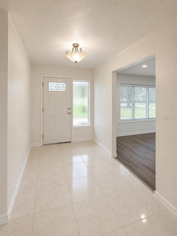 An entryway with light-colored tile flooring, a white front door, and a view into a room — 1221 SW SKATES STREET, ARCADIA, FL