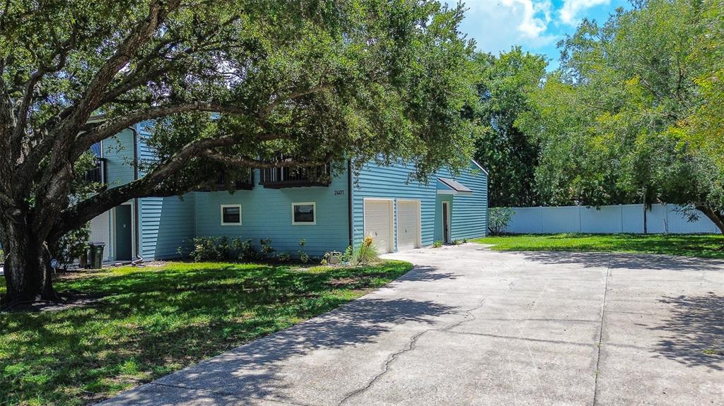 A light blue two-story house with a concrete driveway and a large oak tree — 6334 92ND PLACE N UNIT 2401, PINELLAS PARK, FL