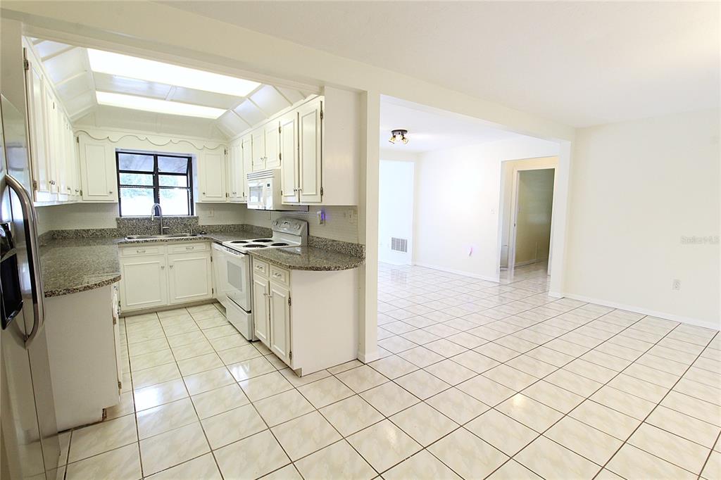 A kitchen with white cabinets and granite countertops opens into a tiled dining area — 2516 E MILMAR DRIVE, SARASOTA, FL