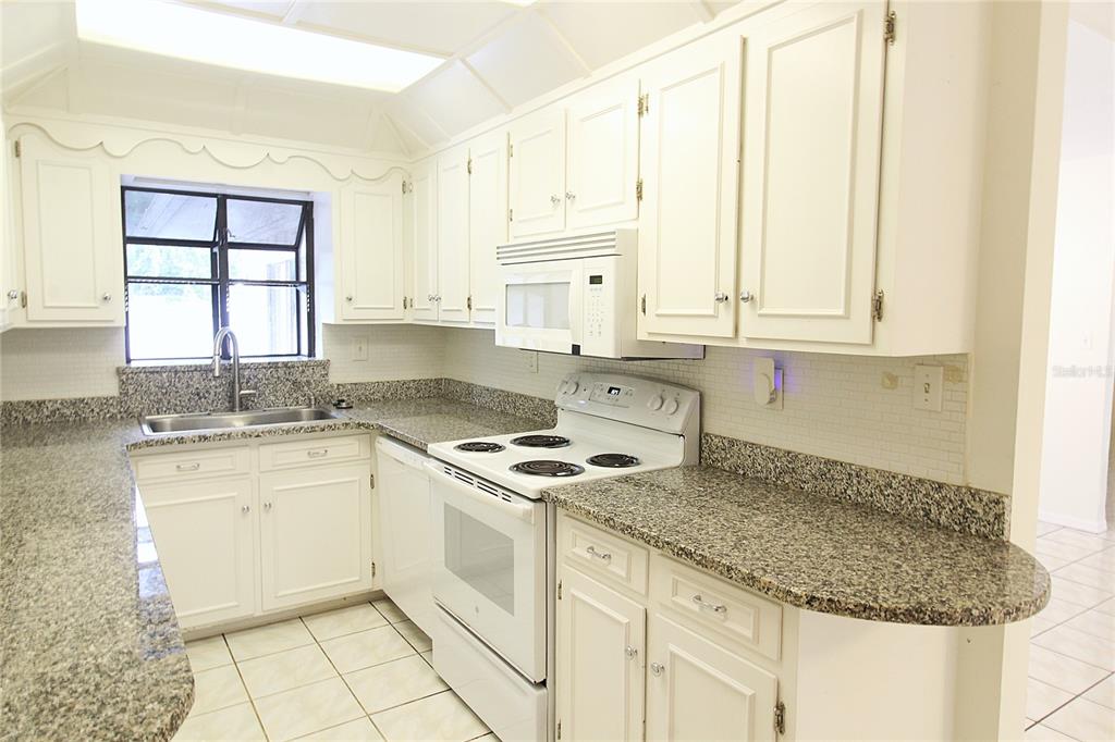 A kitchen with white cabinets, granite countertops, white appliances, and a window above the sink — 2516 E MILMAR DRIVE, SARASOTA, FL