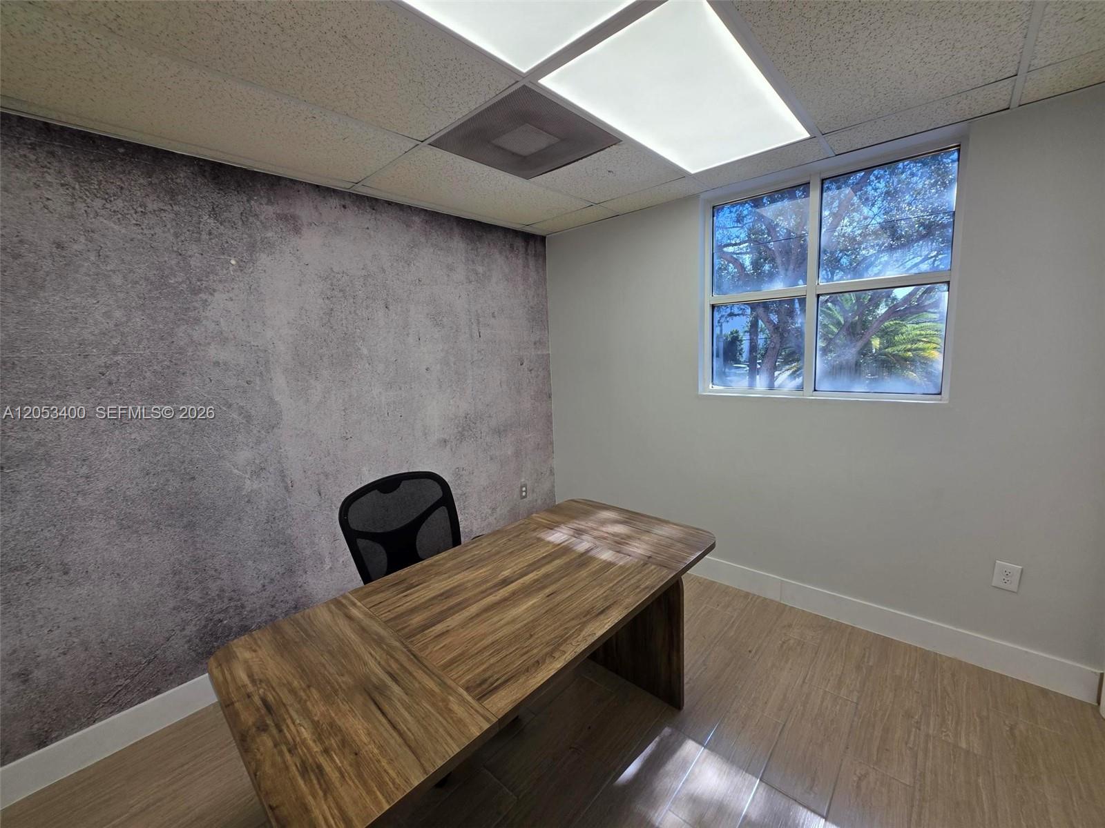 An office features a wood-grain desk, a textured accent wall, and a window with trees — 8555 NW 29th St, Doral FL 33122, DORAL, FL